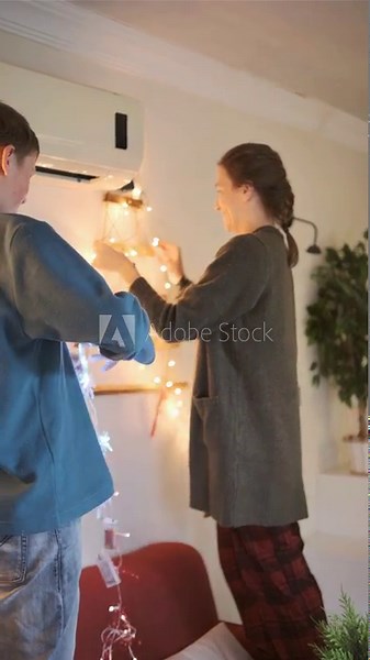 Mother and son decorating room with glowing festive lights, cozy indoor family preparation moment
