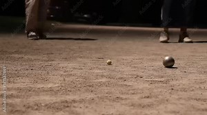 Petanque is popular game. Players throw balls and continue to play even at night with artificial lighting.