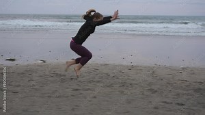 Slow motion dolly shot of female athletes performing cartwheel and backflips at beach