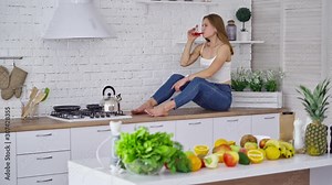 Woman In Modern Combination Of Kitchen. Young woman sitting on table in the kitchen while drinking juice