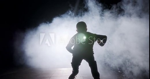 silhouette of a female dancer performing hip hop dance in slow motion with light and smoke background