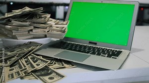 Close up pyramid of stacks 100 US dollars bills of one hundred lying on rotating surface near laptop with chromakey in office night time. Big money and business investment.