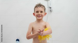 Happy laughing boy playing with yellow sponge while washing under shower in bath. Concept of hygine, children development and fun at home