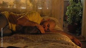 A bearded adult man is lying on the bed and stroking a lop-eared rabbit, communicating with him. Rest and pet care