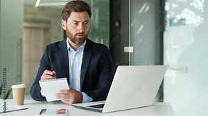 Businessman watching video call online conference taking notes looking at laptop computer screen sitting at workplace in office. Male listening remote business training or course talking with a tutor