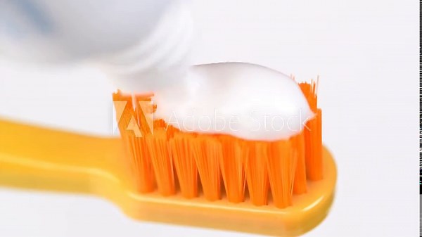 Applying white toothpaste to a orange toothbrush macro video. Dental care concept. Super close up, toothpaste with toothbrush.