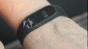 Wristband of heart rate monitor. The woman touches and looks at the wristband of pulse monitor indoors