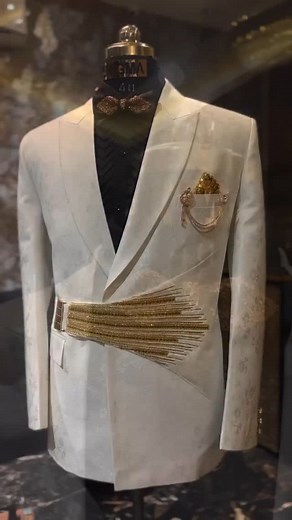 Elevate your presence with this luxurious ivory suit, designed for the man who believes in timeless sophistication with a royal touch. The double-breasted blazer features sleek tailoring, enhanced with golden embroidery accents and a statement waist belt that radiates grandeur. A classic black shirt and embellished bow tie add depth, while the golden pocket chain and brooch complete the regal ensemble. Perfect for weddings, receptions, and red-carpet evenings — this look is pure luxury redefined