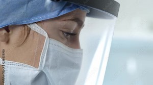 Side view of female nurse working wearing face mask and shield in lab.