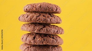 Rotating stack of fresh homemade cookies. Tasty bakery dessert. Pile of oatmeal cookies rotating on yellow background. Brown cookies. Food concept. Close-up in 4K, UHD
