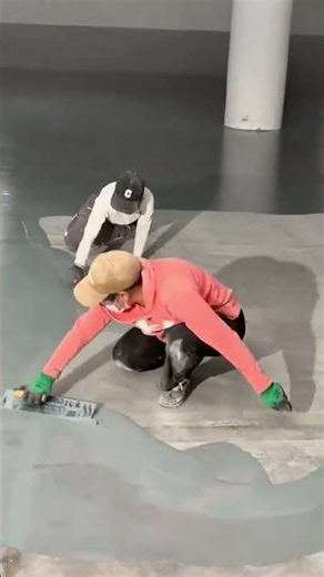 Two workers leveling and smoothing a concrete or plastered floor surface using hand trowels
