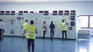 Workers in power plant control room looking at control panel & checking system