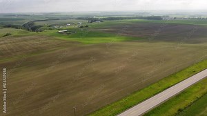Aerial flight over prairie farm fields and a rural highway as moving cloud shadows travel across the landscape in Alberta Canada.