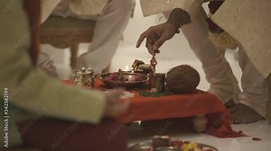 Traditional indian custom for barefoot groom, to pour with tiny golden spoon holy water on the statue on the plate, traditional jars and cutlery, coconut, and other ritual objects