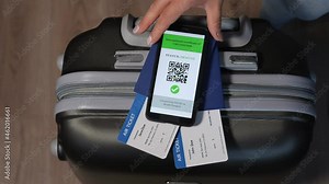 Close-up of a girl puts a phone with a QR code about vaccination against coronavirus on a suitcase with passports and plane tickets.