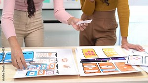 Two female web designers collaborating on a user interface for a mobile phone application. They are reviewing design ideas and discussing the layout