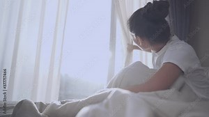 Young adult Asian woman open window curtain to see morning sun light while sitting down bed with beautiful morning sunshine, open bedroom curtains with, view inside home resident domestic bedroom Stock Video