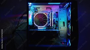 Transparent side panel on the desktop PC case, rainbow RGB illumination on the fans and electronic components inside. Multicolored reflections on the wall.