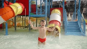Cheerful children are riding down the colorful slide in the waterpark at a summer sunny day
