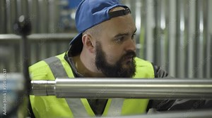Close-up portrait of Caucasian worker with black beard looking at equipment for metal pipes production. Serious man checking manufacturing process. Steel industry, manufacturing. mill.