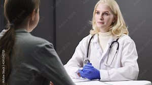 Serious young female doctor talking to a female patient. Checks medical history