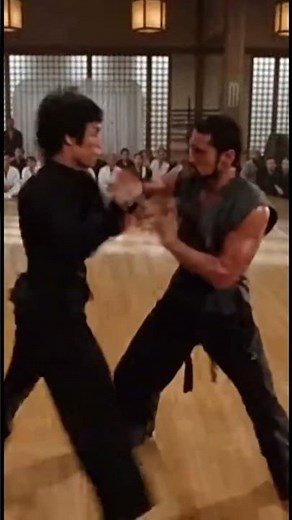 Bruce Lee facing adversary in a dimly lit dojo