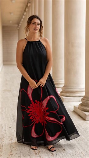 Make an unforgettable entrance in the Francesca Gown, a modern statement of effortless glamour and bold artistry. Crafted from flowing black sheer crepe, this floor-length gown moves beautifully with every step. The halter neckline gathers softly at the collarbone, creating a graceful, open-shoulder silhouette. An oversized red floral motif blooms across the skirt, a striking hand-rendered design that embodies confidence and femininity. The easy, A-line shape skims the body without clinging, off