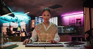Portrait of a Female Software Developer Writing Code in a Creative Office with Neon Lights. Young Woman Focused on Typing on Keyboard and Working on Desktop Computer. Point of View of Screen Monitor