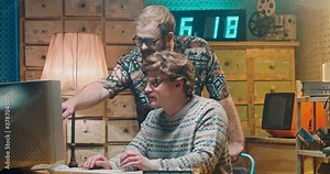 Two Caucasian males friends nerds from 80's working and talking at old PC monitor. Men funny hackers or programists from 70's discussing something at computer. Vintage interior. Retro style.