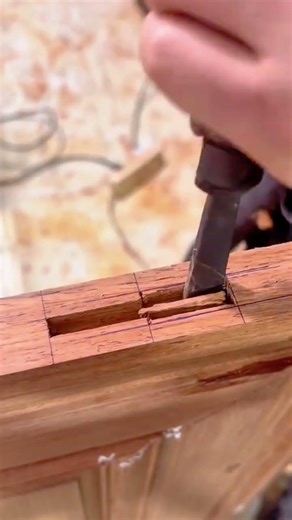 carving the rectangular hole into the brown wood material using a sharp metal chisel tool manually