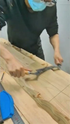 shaving a long wooden plank with a drawknife tool to create a smooth surface on a workbench