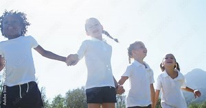 School kids holding hands and jumping in park