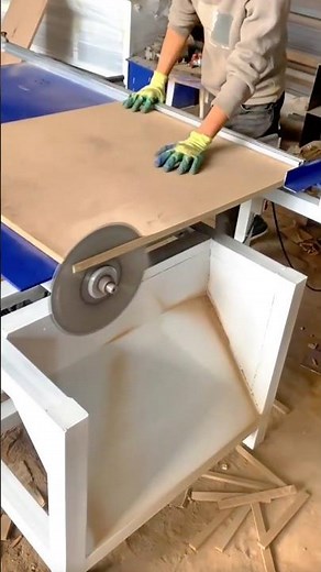 Woodshop worker accurately cutting large MDF board using a circular table saw in a factory