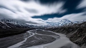 Download Vast Alaskan Mountain Range with Meandering River and Streaking Clouds. for free