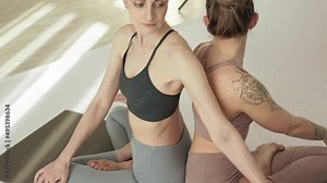 two women practice partner yoga, twist yoga in a light studio