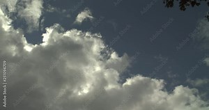 Dramatic rolling clouds, building cloud with skyline. Dark dramatic rain clouds passing. White puffy, fluffy, cumulus clouds rolling across the blue sky during cloudy summer day occluding the sun. Cl