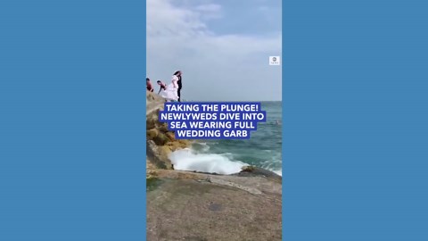 Bride and groom dive into the ocean in wedding outfits