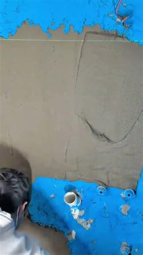 applying a thick layer of wet grey concrete onto a bright blue bathroom wall using a metal scraper