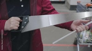 Girl in building store chooses a hand saw. She removes protection from iron teeth and checks how tool is sharpened. Concept of women independence, feminism, gender equality, repair and construction