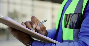 Checklist and man hands, construction worker or building contractor in civil engineering inspection for safety compliance. Urban city, planning and builder person writing notes for architecture job