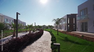 Modern luxury villas line landscaped walkway in upscale residential complex. Property investment options showcased in sunny setting.
