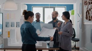 Multi ethnic group of architects working with blueprints and building model on table to design construction layout together. People doing teamwork on architectural urban project.
