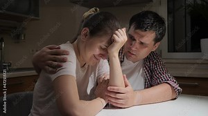 Upset and stressed woman crying and hugging her husband on kitchen at night. Concept of despair, stress, depression, anxiety, family problems, divorce and frustration.