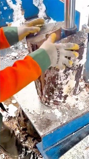 Hydraulic press splitting frozen log while worker wears gloves