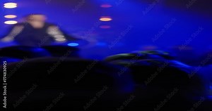 A vertical video showing at fashion week in a dark hall with blue shades. A female model in an ultra fashionable black suit with shiny sleeves walks along the catwalk among the audience. 4k footage