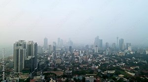 Colombo skyline drone footage at dusk. High-rise towers loom over urban landscape. Coastal cityscape under hazy sky in Sri Lanka. Aerial view includes landmarks, residential areas, sea horizon.