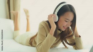 Close -up. Listening to music through her headphone an attractive young Asian woman spontaneously begins to sway and dance to the music while lying on the bed.