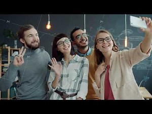 Group of colleagues taking selfie in office using smartphone camera posing with hand gestures