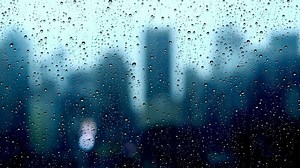 Rain drops pouring down on window glass with urban city skyline view on a rainy weather day