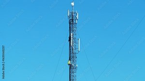 Two workmen on a cell tower. Maintenance staff at the work. High-altitude work. Cell tower on blue background. Repairmen service a cell tower